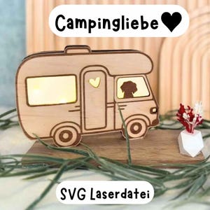 May include: A wooden cutout of a camper van with a heart in the window and a dog silhouette in the driver's seat. The cutout is on a wooden base with the text "Campingliebe" and a heart above the camper and "SVG Laserdatei" below the base.