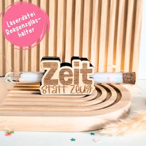 Puede incluir: Porta-tubos de ensayo de madera con las palabras "Zeit statt Zeug" grabadas en él. El soporte está hecho de madera natural y tiene un borde negro. Un tubo de ensayo con un tapón de corcho se inserta en el soporte. El tubo de ensayo está lleno de confeti de colores.