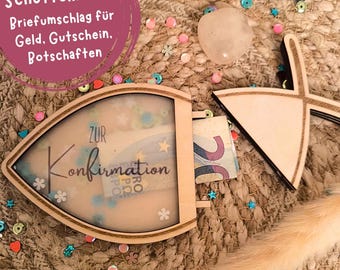 Puede incluir: Una caja de madera con forma de pez con una tapa transparente, decorada con purpurina y las palabras "Zur Konfirmation". La caja está abierta, revelando un billete de 20 euros en su interior. La caja está sobre una superficie marrón y beige con confeti de colores.