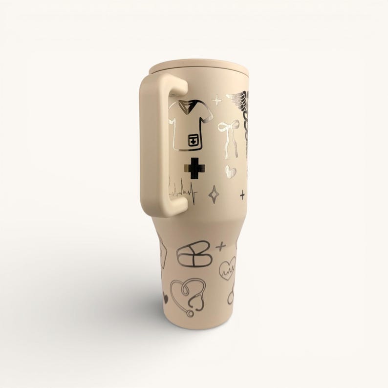 May include: A beige insulated tumbler with a handle, adorned with silver medical-themed illustrations. The design includes a nurse's uniform, a cross, a stethoscope, and a heartbeat line. The tumbler is designed to keep beverages cold or hot.