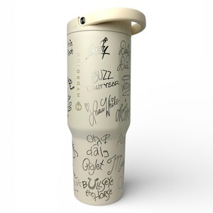 Puede incluir: Vaso aislado de color crema con asa y tapa de rosca. El vaso est&aacute; cubierto con escritura negra, incluidas las palabras "Buzz Lightyear" y otros nombres de personajes. La palabra "HYDROJUG" est&aacute; impresa verticalmente en el lateral.