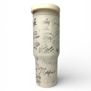 Puede incluir: Una botella de agua Hydrojug de color crema con tapa blanca. La botella est&aacute; cubierta de firmas plateadas de personajes de Disney, como Woody, Daisy Duck y Mal&eacute;fica. La palabra "HYDROJUG" est&aacute; impresa en la tapa.