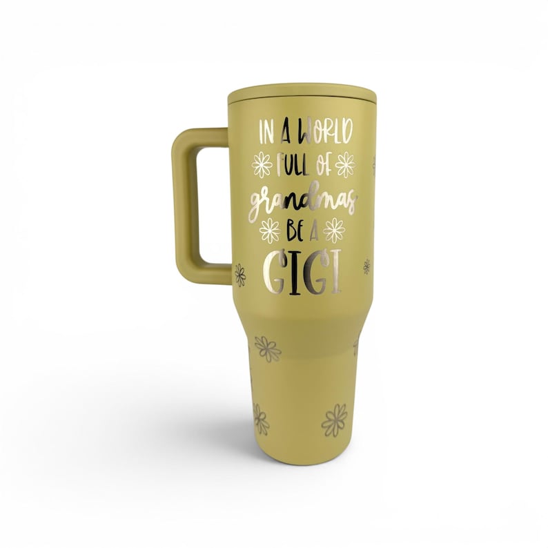 May include: A matte olive green insulated tumbler with a handle and a lid. The front features silver text that reads IN A WORLD FULL OF GRANDMAS BE A GIGI, surrounded by small silver flower icons scattered across the body of the drinkware.