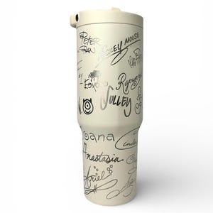 Puede incluir: Vaso t&eacute;rmico de color crema con tapa y asa. El vaso est&aacute; cubierto de firmas plateadas de varios personajes, como Mickey Mouse, Peter Pan y Ariel. Dise&ntilde;ado para mantener las bebidas calientes o fr&iacute;as.