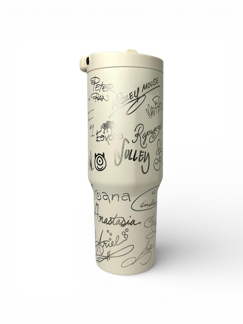 Puede incluir: Vaso t&eacute;rmico de color crema con tapa y asa. El vaso est&aacute; cubierto de firmas plateadas de varios personajes, como Mickey Mouse, Peter Pan y Ariel. Dise&ntilde;ado para mantener las bebidas calientes o fr&iacute;as.
