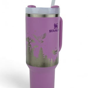 Puede incluir: Un vaso Stanley lila con tapa y pajita blancas. Tiene un gr&aacute;fico plateado de una escena de bosque con un mago, un b&uacute;ho y estrellas. El asa es lila y el logotipo de Stanley es visible.