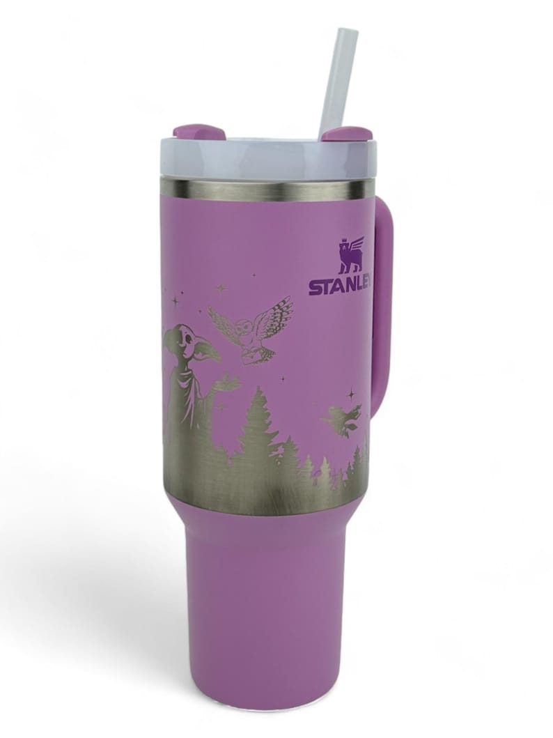 Puede incluir: Un vaso Stanley lila con tapa y pajita blancas. Tiene un gr&aacute;fico plateado de una escena de bosque con un mago, un b&uacute;ho y estrellas. El asa es lila y el logotipo de Stanley es visible.