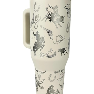 Puede incluir: Taza de viaje color crema con asa, con un dise&ntilde;o tem&aacute;tico de vaquero. Las ilustraciones incluyen vaqueros, herraduras, sombreros, un toro y las palabras "Cowboy" y "Yeehaw".