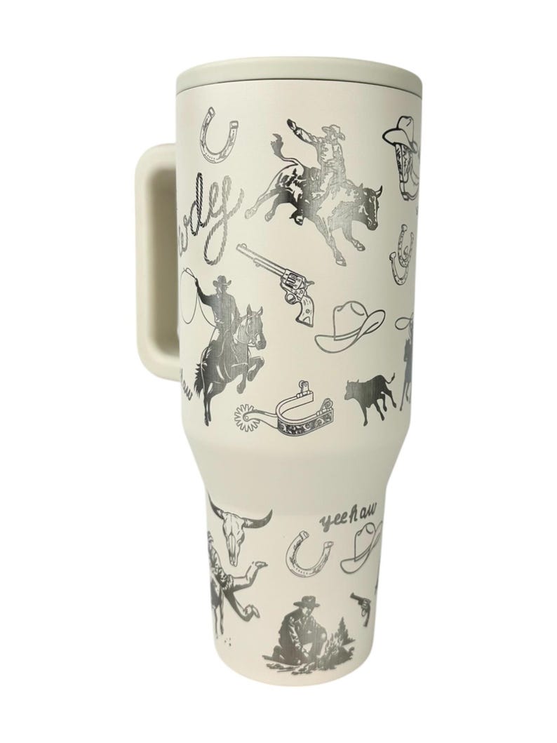Puede incluir: Taza de viaje color crema con asa, con un dise&ntilde;o tem&aacute;tico de vaquero. Las ilustraciones incluyen vaqueros, herraduras, sombreros, un toro y las palabras "Cowboy" y "Yeehaw".