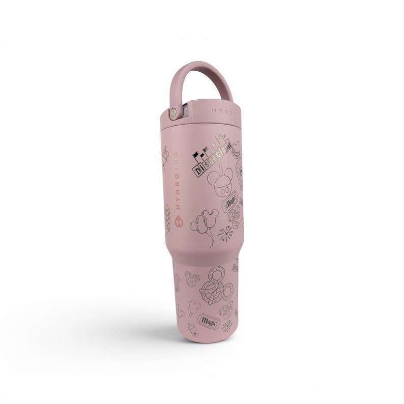 May include: A dusty rose-colored insulated tumbler with a matching handle and lid. The exterior features a repeating pattern of line-art icons including a castle, mouse ears, balloons, and tickets, with the text Disneyland and Magic printed on it.