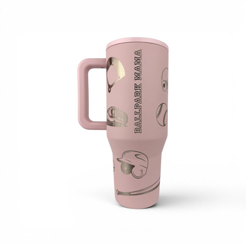 May include: A light pink insulated tumbler with a handle, featuring metallic gold baseball-themed graphics including a diamond, glove, ball, helmet, and bat, with the text BALLPARK MAMA printed vertically in a bold, dark sans-serif font.