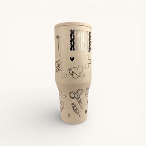 May include: A beige tumbler with a lid, adorned with black medical-themed doodles and the word "NURSE" in a stacked design. The tumbler features a variety of illustrations, including a heart, cross, scissors, and syringe.