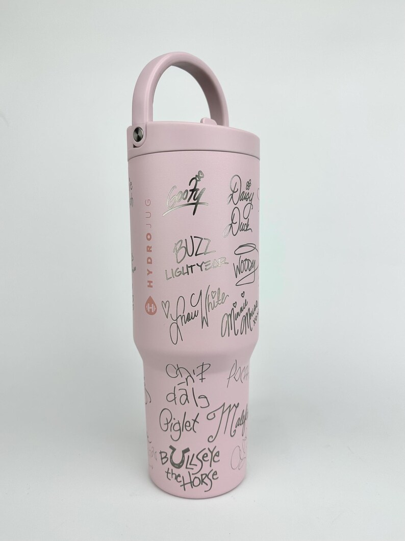 Puede incluir: Una botella de agua Hydro Jug de color rosa claro con asa y tapa de rosca. La botella est&aacute; cubierta de firmas negras y nombres de personajes, incluyendo "Goofy", "Buzz Lightyear" y "Blancanieves".