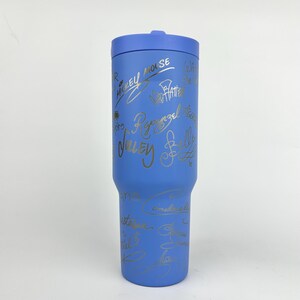 Puede incluir: Un vaso azul con tapa a juego. El vaso est&aacute; cubierto de firmas doradas, incluyendo "Mickey Mouse" y "Rapunzel". El vaso est&aacute; dise&ntilde;ado para mantener las bebidas fr&iacute;as o calientes. Un art&iacute;culo de bebida elegante y funcional.