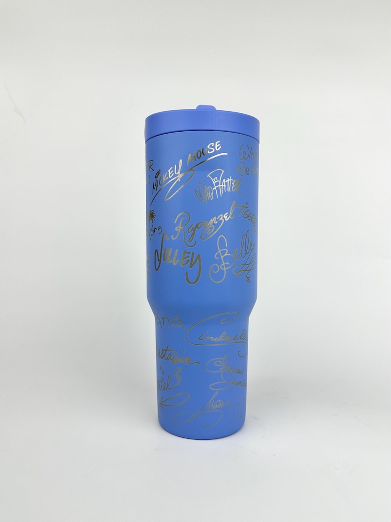 Puede incluir: Un vaso azul con tapa a juego. El vaso est&aacute; cubierto de firmas doradas, incluyendo "Mickey Mouse" y "Rapunzel". El vaso est&aacute; dise&ntilde;ado para mantener las bebidas fr&iacute;as o calientes. Un art&iacute;culo de bebida elegante y funcional.