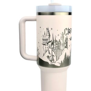 Puede incluir: Un termo de viaje rosa claro con asa, tapa blanca y pajita. El termo presenta una ilustraci&oacute;n en blanco y negro de un castillo con la palabra "Clair". Dise&ntilde;ado para mantener las bebidas fr&iacute;as o calientes.