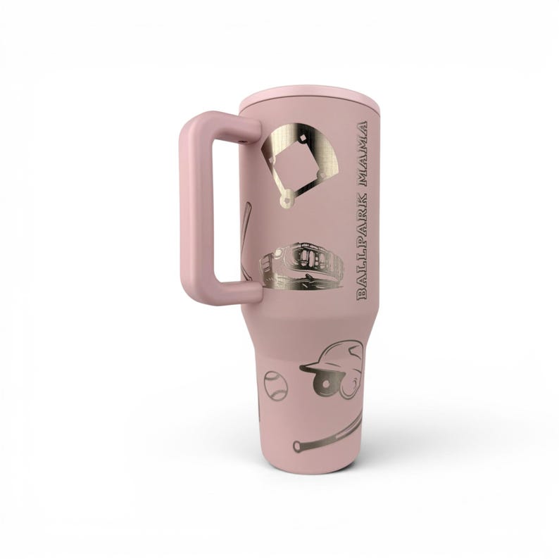 May include: A light pink tumbler with a handle featuring metallic gold baseball-themed graphics including a diamond field, a glove, a bat, a helmet, and a ball. The text BALLPARK MAMA is printed vertically in gold lettering on the side of the cup.