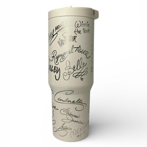 Puede incluir: Un vaso de color crema con tapa a juego. El vaso est&aacute; cubierto de firmas manuscritas negras de personajes de Disney, como Mickey Mouse, Winnie the Pooh y Cenicienta. El vaso est&aacute; dise&ntilde;ado para mantener las bebidas fr&iacute;as o calientes.