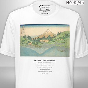 May include: White t-shirt featuring a Japanese landscape print. The artwork depicts a mountain, lake, and trees in shades of blue, green, and beige. Text at the bottom reads "Reflections in Lake at Misaka in Kai Province".