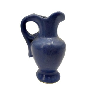 May include: A small, blue ceramic pitcher with a handle. The pitcher has a rounded body and a spout for pouring. The handle is arched, and the pitcher is a solid, matte blue color. The pitcher is likely for decorative use.