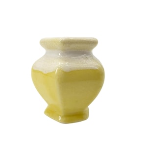 May include: A small, yellow ceramic vase with a square base and a rounded top. The top of the vase is white with a textured appearance. The vase has a unique, geometric shape and is suitable for small floral arrangements or decorative purposes.