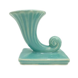 May include: A turquoise ceramic vase with a horn-like shape and a square base. The vase has a fluted design on the top and a curled end. The overall design is reminiscent of a cornucopia.