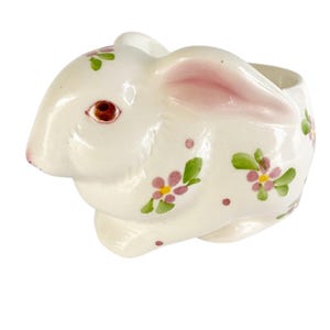 May include: A white ceramic bunny planter with pink and green floral details. The bunny has a pink nose and a small opening on the top for planting.