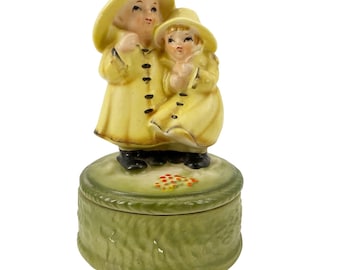 Caja de música de cerámica vintage con niños en impermeables, color amarillo y verde, fabricada en Japón. Necesita reparación.