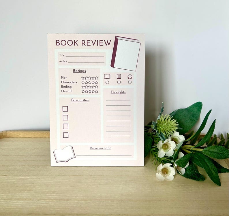May include: A light pink book review notepad with the words "BOOK REVIEW" at the top. The notepad includes sections for title, author, ratings, favorites, and thoughts. A small book illustration is at the bottom.