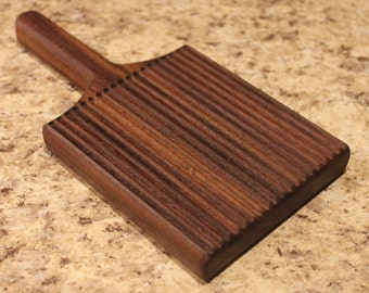 May include: A dark brown wooden butter paddle with a handle and a grooved surface.