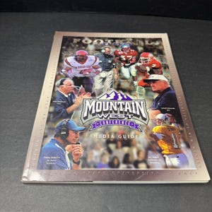 以下が含まれることがあります： マウンテンウェストカンファレンスのメディアガイド。フットボール選手とコーチが特集されています。表紙には「Mountain West Conference Media Guide」の文字が入った紫と白のロゴがあります。ガイドにはチームの写真と大学名が含まれています。