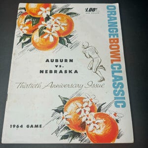 May include: Vintage Orange Bowl Classic program cover featuring illustrations of oranges and a football player. The cover reads "Auburn vs. Nebraska" and "Thirtieth Anniversary Issue" with the 1964 game date.