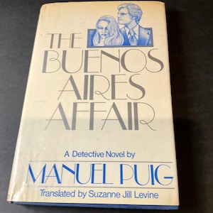 May include: A vintage paperback book titled "The Buenos Aires Affair" by Manuel Puig. The cover features a blue illustration of a man and woman, with the title in large, silver letters.