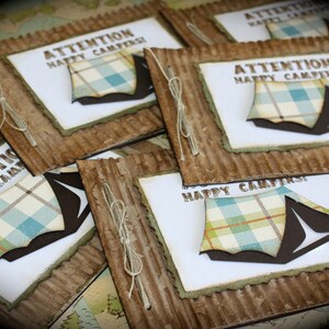 May include: A stack of brown cardstock cards with a white background and a blue and white plaid tent design. The text on the cards reads "Attention Happy Campers!"