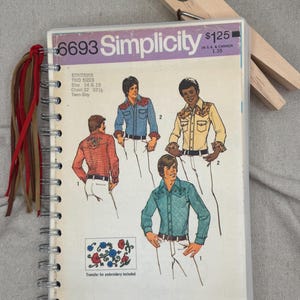 May include: A spiral-bound notebook featuring a vintage Simplicity 6693 sewing pattern cover. The cover displays illustrations of three shirts with western-style yokes, embroidery details, and the text '6693 Simplicity'. Red and brown suede tassels are attached to the silver metal spiral binding.