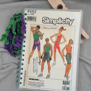 May include: A spiral-bound Simplicity sewing pattern booklet, number 8562, size SM, featuring illustrations of athletic apparel. The cover displays four figures in activewear, the text Surf Club, and a green and purple ruffled fabric trim attached.