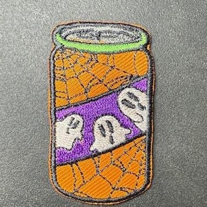 Könnte beinhalten: Ein orangefarbener und violetter gestickter Aufnäher mit einer Soda-Dose mit Spinnennetz-Design und drei Geistern.