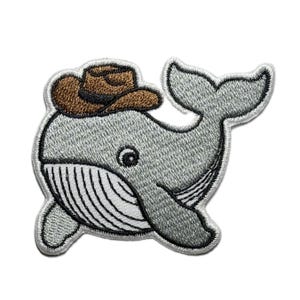 Puede incluir: Parche bordado para planchar de una ballena gris con un sombrero de vaquero marrón. La ballena tiene la barriga blanca con rayas negras y un contorno negro.