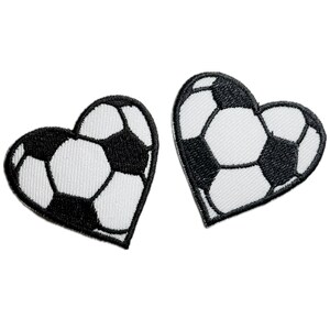 May include: Two black and white embroidered patches shaped like hearts. Each heart features a soccer ball design.
