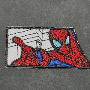 May include: Embroidered patch featuring Spider-Man in a dynamic pose. The patch showcases the character's iconic red and blue suit, with intricate detailing. The background depicts a web design in gray, with a black border.