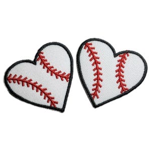 May include: Two white heart-shaped patches with red stitching, resembling a baseball, are shown against a white background.