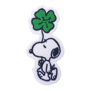 Puede incluir: Parche blanco bordado de Snoopy sosteniendo un trébol de cuatro hojas verde.