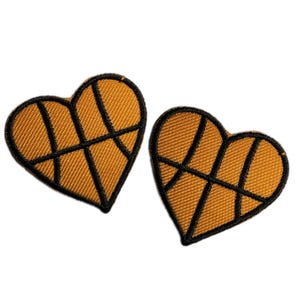 Pode incluir: Dois patches de feltro marrom em forma de coração com costuras pretas, cada um representando uma bola de basquete.