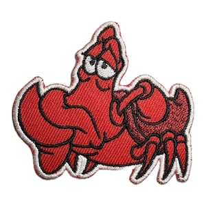 May include: Red embroidered iron-on patch of Sebastian the crab from Disney's The Little Mermaid. Sebastian is shown with his signature grumpy expression and is wearing a red shell.