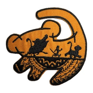May include: An orange embroidered patch depicting the silhouette of a lion in a sleeping pose. The lion's mane is outlined in black and the background features a black silhouette of a savanna scene with trees and animals.