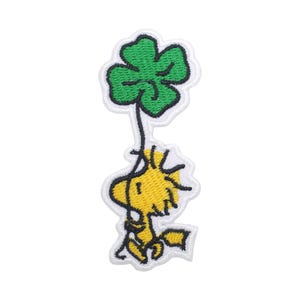 Può includere: Toppa ricamata raffigurante un uccello giallo dei cartoni animati che tiene in mano un quadrifoglio verde. La toppa ha un bordo bianco. L'uccello sorride e sembra fluttuare. La toppa è probabilmente per abbigliamento o accessori.