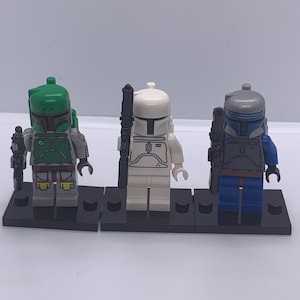 Puede incluir: Tres minifiguras LEGO Star Wars, Boba Fett, un Stormtrooper y un Mandaloriano, de pie sobre placas base negras. Boba Fett lleva un casco y una armadura verdes, el Stormtrooper lleva un casco y una armadura blancos, y el Mandaloriano lleva un casco y una armadura azules.