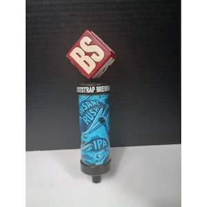 May include: A beer tap handle with a red and white square top featuring the letters "BS". The cylindrical body is blue with the words "INSANE RUSH" and "IPA". The tap handle is designed for Bootstrap Brewing.
