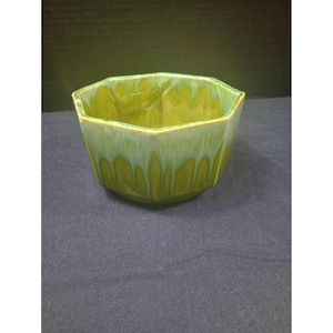 May include: A green ceramic bowl with a unique octagonal shape. The bowl has a glossy finish with a two-tone effect, featuring a darker green base that fades into a lighter, dripped-down green color. The bowl is likely vintage.