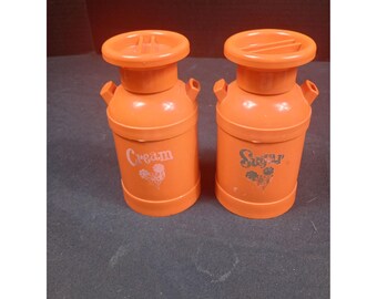 Dispensadores de leche con forma de lata de naranja, crema y azúcar, estilo vintage retro kitsch de mediados de siglo.